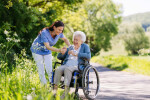 Female caregiver and senior woman in wheelchair picking wild flowers